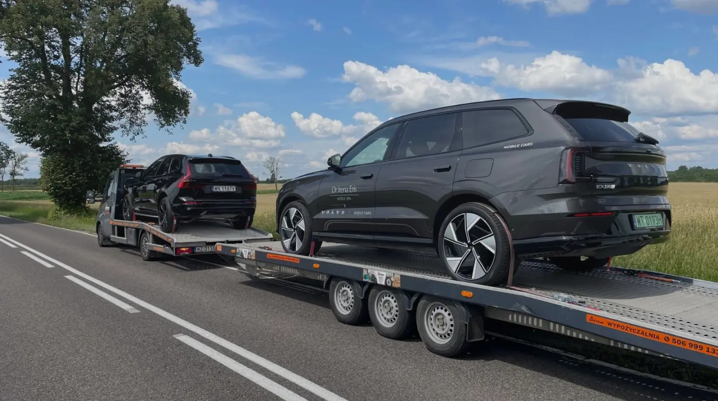 Czarny samochód osobowy transportowany na lawecie po drodze wśród pól