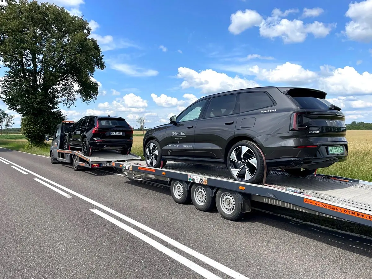 Ciemny SUV i drugi samochód na lawecie, w trakcie transportu drogą