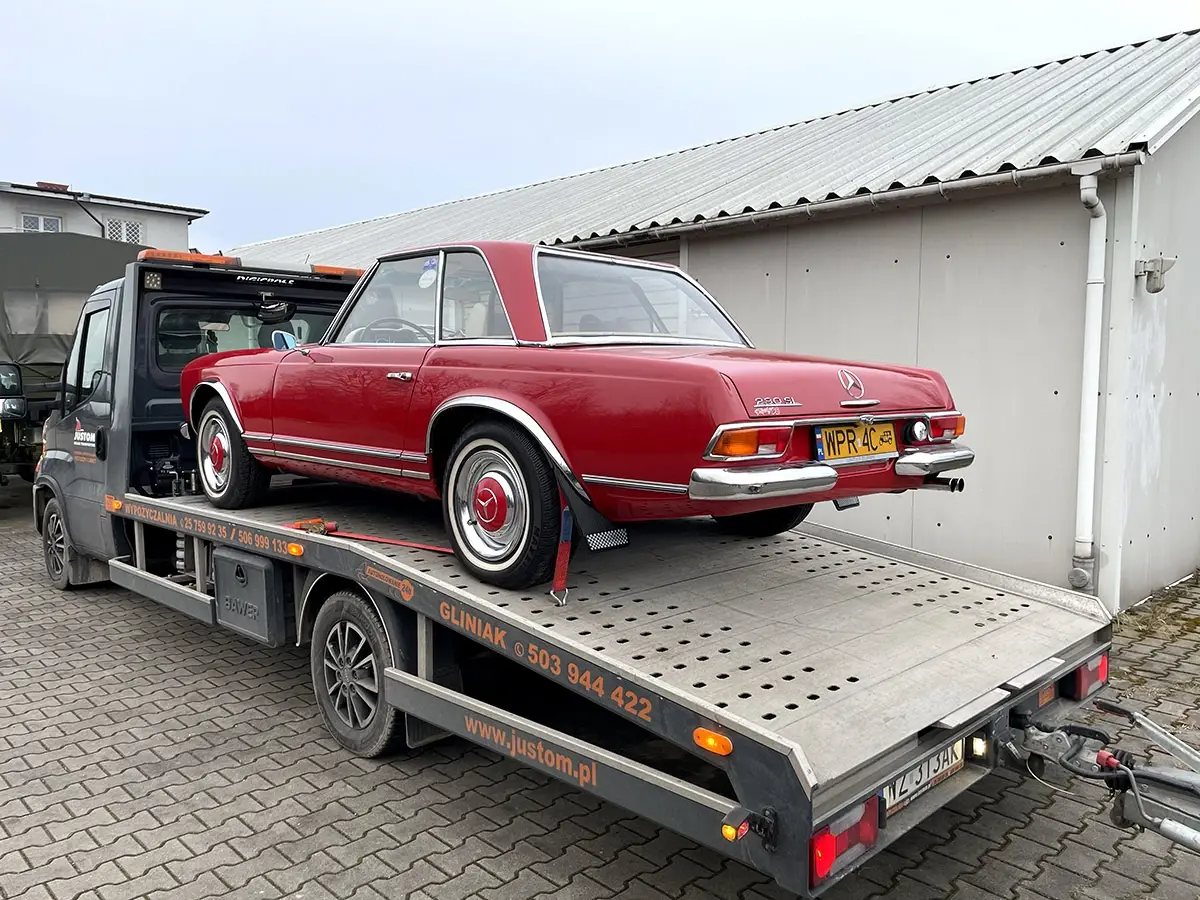 Czerwony zabytkowy Mercedes załadowany na lawetę pod wiatą