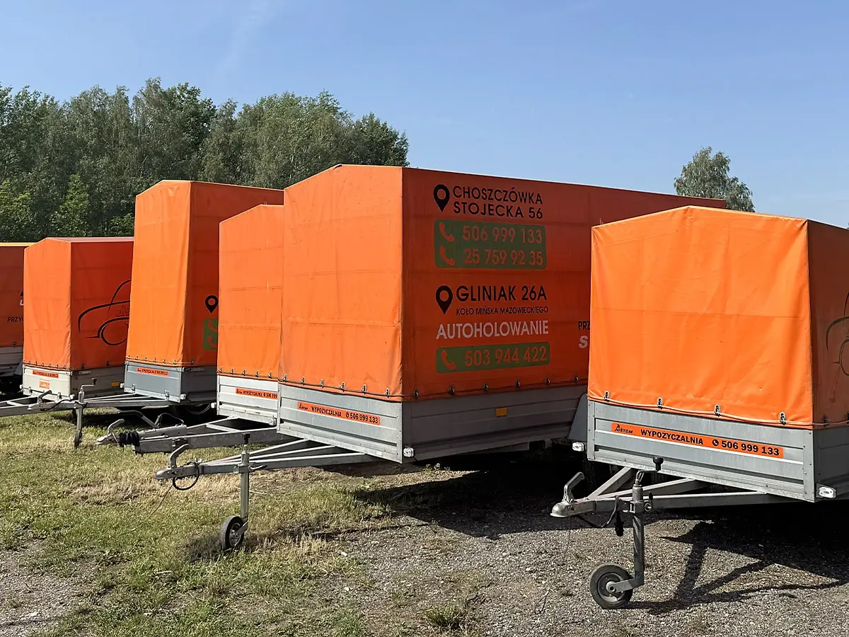 Pomarańczowe przyczepy z plandeką ustawione rzędem na placu