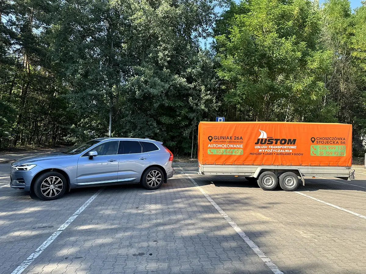 Samochód osobowy z podłączoną przyczepą z plandeką na parkingu