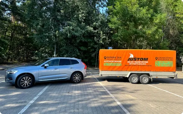 Samochód z przyczepą Justom zaparkowany na parkingu.